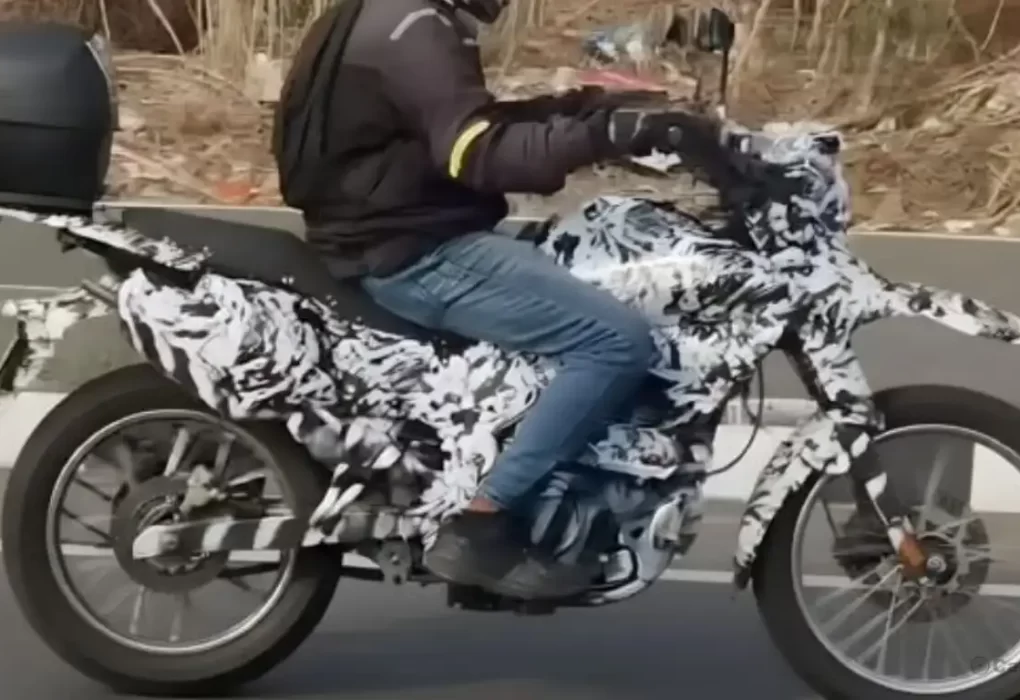 A heavily camouflaged Bajaj dual-sport motorcycle undergoing road testing in India, showcasing a high front beak and spoked wheels.