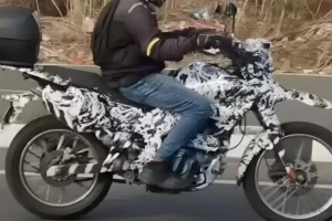 A heavily camouflaged Bajaj dual-sport motorcycle undergoing road testing in India, showcasing a high front beak and spoked wheels.