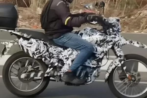 A heavily camouflaged Bajaj dual-sport motorcycle undergoing road testing in India, showcasing a high front beak and spoked wheels.