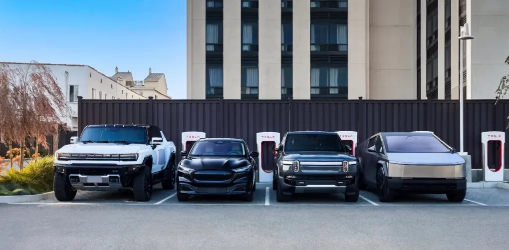 A modern, multi-stall public EV charging hub with a mix of DC fast chargers and Level 2 plugs bustling with different electric vehicles in a retail parking lot.