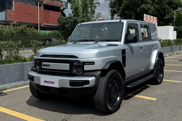 Front three-quarter view of the silver iCaur V23 electric SUV on a road in Nepal, showing its retro boxy design, round LED headlights, and rugged bumper.