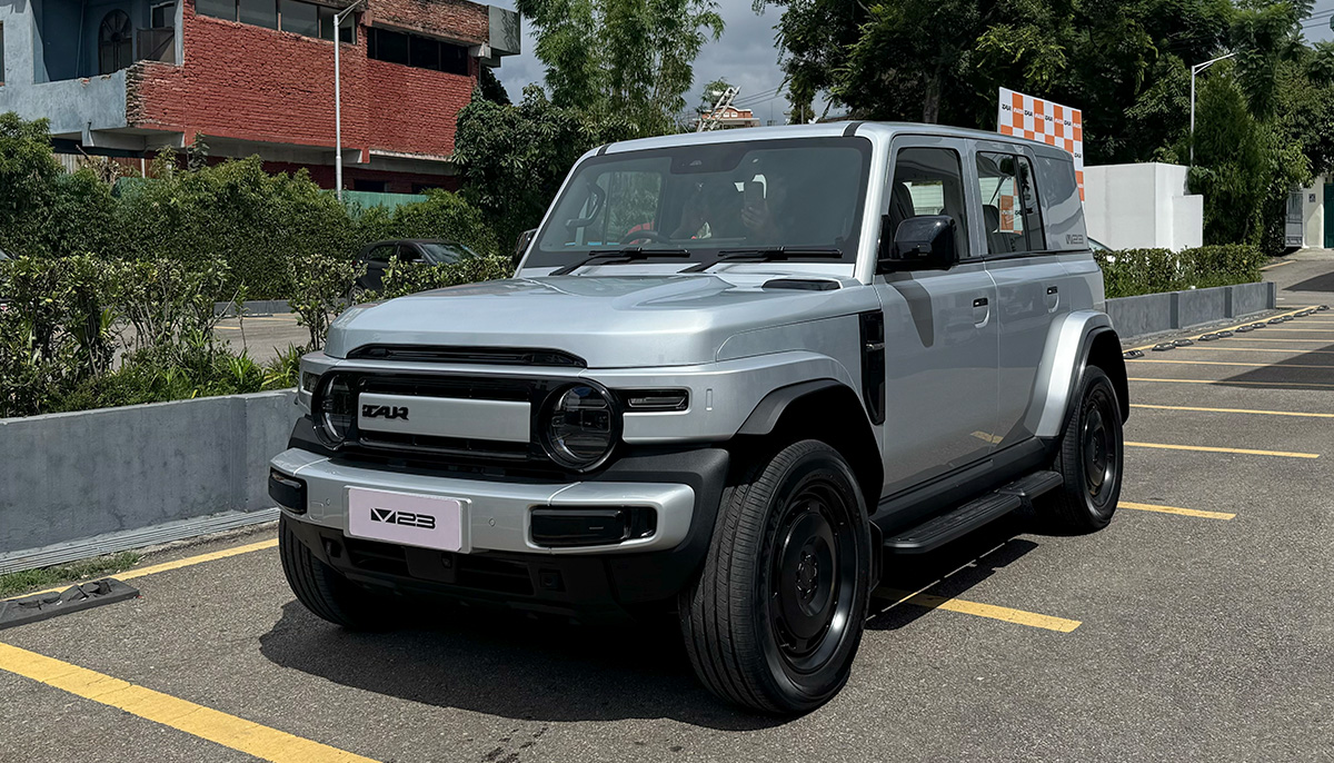 Front three-quarter view of the silver iCaur V23 electric SUV on a road in Nepal, showing its retro boxy design, round LED headlights, and rugged bumper.