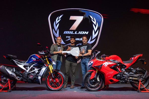 A premium black TVS Apache RR 310 motorcycle being delivered to a customer at a flagship showroom celebrating a global milestone.